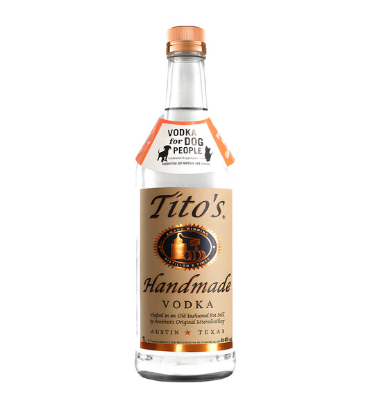 Tito’s Handmade Vodka 1L clear glass bottle on white background, cream label with black text and copper dog logo